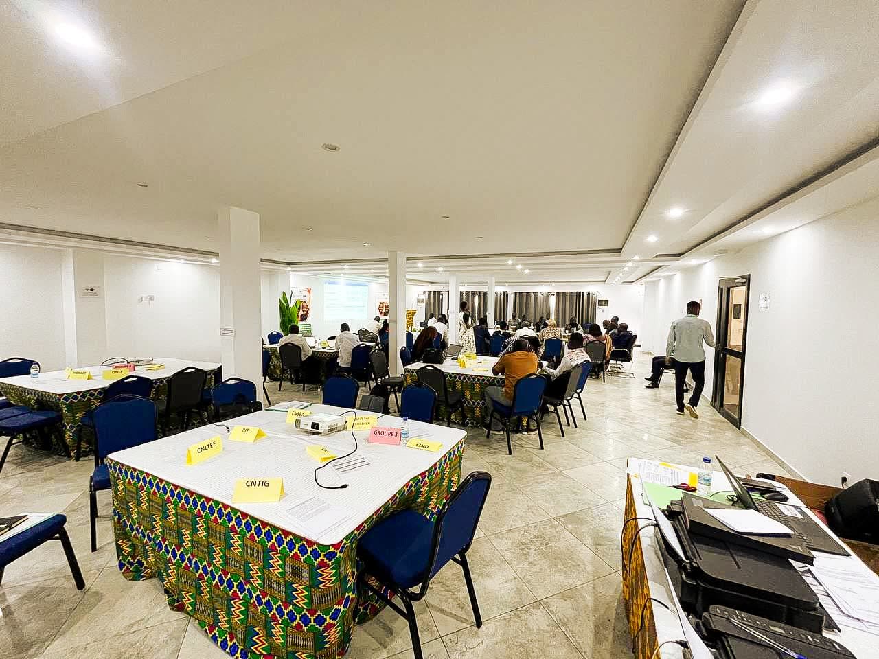 Séminaire en séance plénière dans la grande salle de NH Le Rêve, participants répartis en tables de groupe