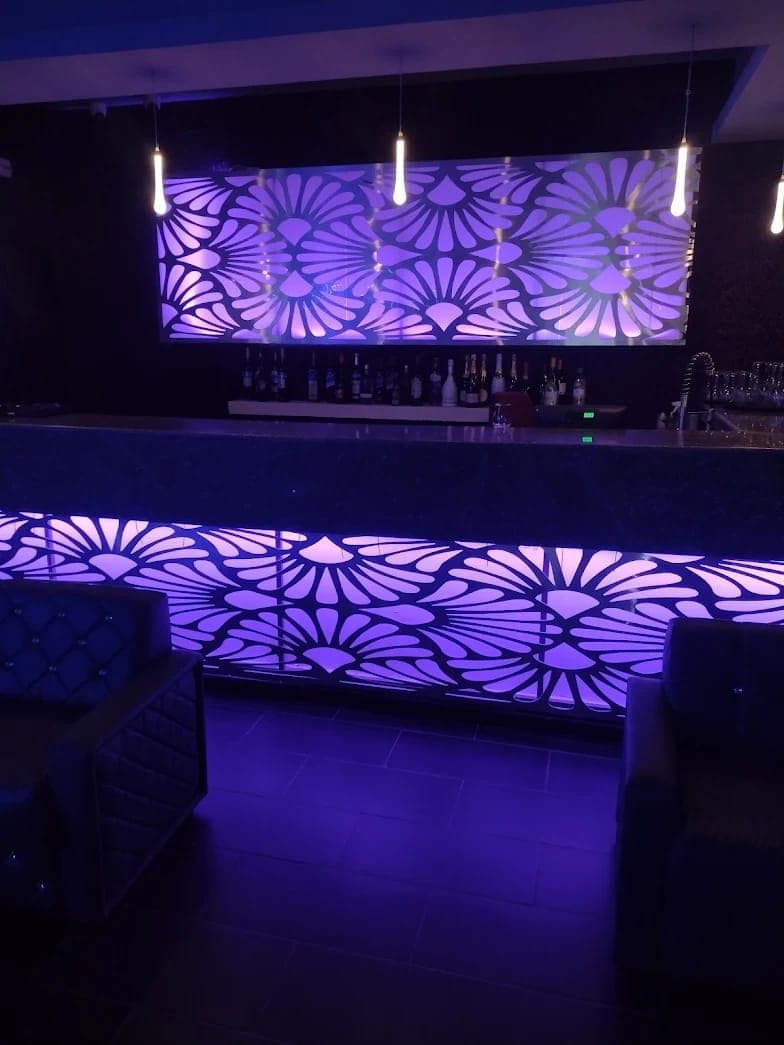 Comptoir du bar de NH Le Rêve illuminé, panneaux lumineux violets et sélection de bouteilles